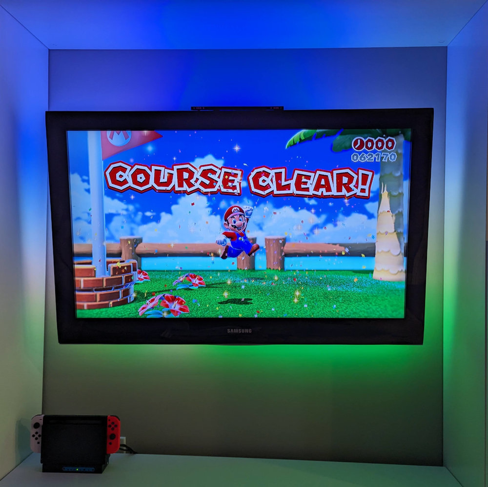 The TV mounted on the wall, showing a Mario game being played